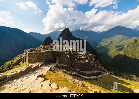 Machu Picchu teilweise durch das letzte Sonnenlicht beleuchtet. Weitwinkel-Blick von den Terrassen mit malerischen Himmel und leuchtende Pfad Stockfoto