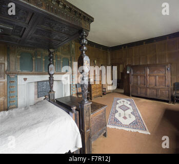 Henry Ferrers Schlafzimmer, Baddesley Clinton, Warwickshire. Die Schnitzereien und Intarsien Himmelbett Eiche Bettgestell erfolgte vom siebzehnten Jahrhundert Fragmente, die im 19. Jahrhundert zusammengestellt wurden. Der Kaminsims enthält die Wappen der Ferrers G Stockfoto