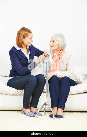 Lächelnde Frau im Gespräch mit älteren Frau mit Rohrstock zu Hause Stockfoto