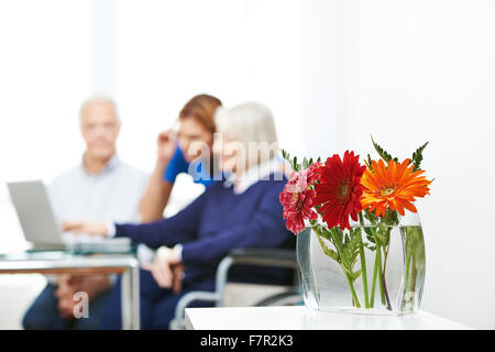 Gerbera Blumen in Vase mit Senioren mit Computer im Hintergrund Stockfoto