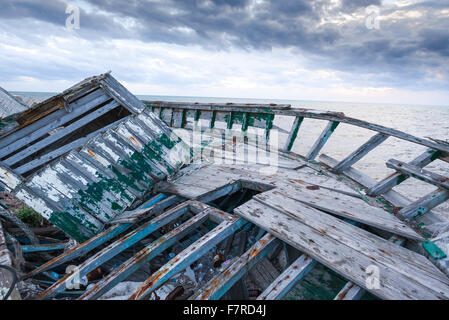 Verlassenes Flüchtlingsboot, Blick auf ein verlassenes Flüchtlingsboot, das dem Verfall überlassen wurde, neben der Meeresmauer in Marsala, Sizilien. Stockfoto