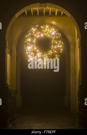 Riesige Adventskranz, Glühen mit Lichterketten und hängend von einem Torbogen am Polesden Lacey, Surrey. Stockfoto