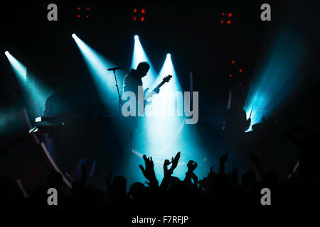 E-Gitarre Spieler von Rock Band in blau im Rampenlicht während Pop Konzert mit Silhouette der Masse Stockfoto