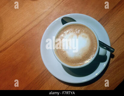 kleine Cappuccino-Tasse auf Tisch mit herzförmigen Schaum und Löffel Stockfoto