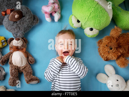 Fröhlicher einjähriger Junge liegend mit vielen Plüschtiere Stockfoto