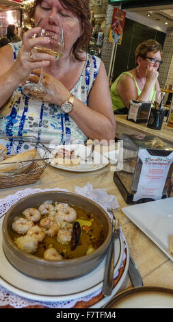 Portion Gambas in Knoblauch Öl und eine Frau trinkt ein Glas Weißwein in einer Tapas Bar in Spanien Stockfoto