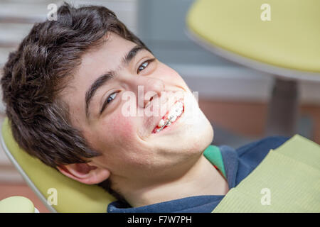 Kaukasische Teenager mit Aknehaut liegend auf dem Zahnarztstuhl lächelt mit Klammern Stockfoto