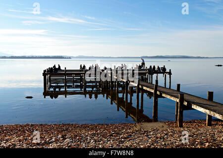 Menschen sitzen auf hölzernen Pier am See, Feldwieser Bucht, Chiemsee, Oberbayern, Deutschland, Europa. Stockfoto