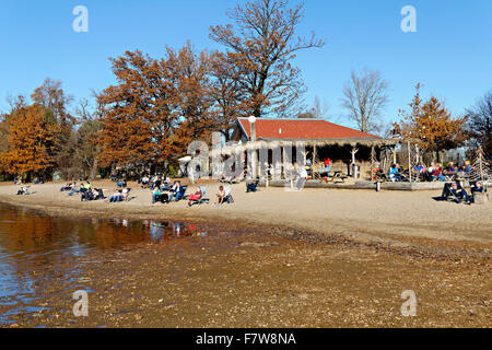 Menschen entspannen am Strand Vorland mit Shop und Bier Garten in der Ferne Feldwieser Bucht, Chiemsee, Oberbayern, Deutschland, Stockfoto