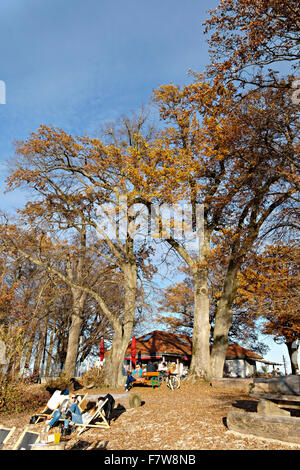 Menschen entspannen am Strand Vorland mit Shop und Bier Garten in der Ferne Feldwieser Bucht, Chiemsee, Oberbayern, Deutschland, Stockfoto