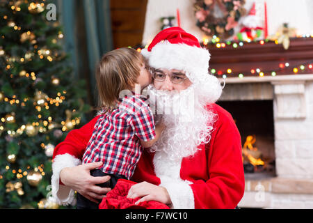 Santa Claus und Kind junge. Kind erzählt seinem Weihnachtswunsch in Santa Claus in der Nähe der Weihnachtsbaum gegenüber Kamin Stockfoto