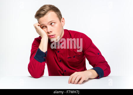 Gelangweilt müder junger Mann im roten Hemd sitzt und wegsehen isoliert auf weißem Hintergrund Stockfoto