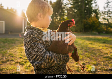 Junge, der im Garten steht und ein Huhn hält Stockfoto