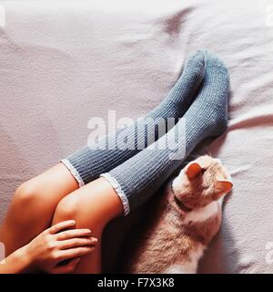 Frauenbeine in langen Socken und Katze auf einem Bett liegend Stockfoto