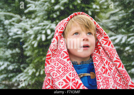 Junge, eingewickelt in eine Decke im Schnee nachschlagen Stockfoto