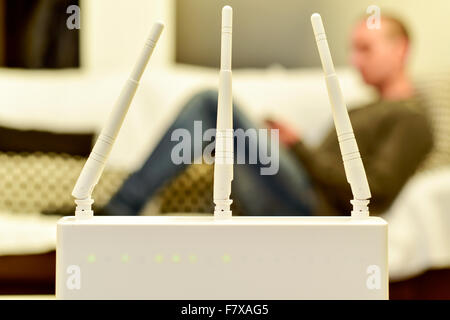 Nahaufnahme von einem wireless-Router und ein junger kaukasischen Mann mit einem Smartphone auf einer Couch im Hintergrund Stockfoto