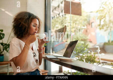 Schuss der junge Frau in einem Café mit Laptop sitzen und Kaffee trinken. Afroamerikanische Mädchen heiß und frisch Kaffeetrinken Stockfoto