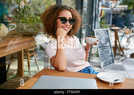 Porträt von schönen jungen Mädchen, die mit einer Tasse Kaffee im Café. Stilvolle junge afrikanische Mädchen trinken Kaffee im Straßencafe. Stockfoto