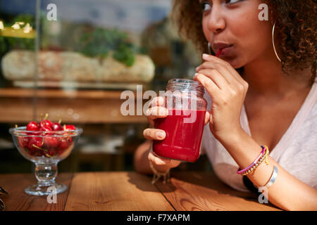 Schließen Sie herauf Bild der jungen Afrikanerin trinken Saft aus frischen Früchten beim Sitzen am Café im Freien. Stockfoto