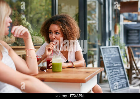 Afrikanische Mädchen trinken Saft während des Chattens mit ihrer Freundin im Straßencafé. Freundinnen treffen in Outdoor-Café Stockfoto