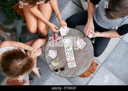 Draufsicht der drei Jugendlichen Spielkarten im Straßencafé. Die Jugendlichen an einem Kaffee-Tisch sitzen und spielen Kartenspiel. Stockfoto
