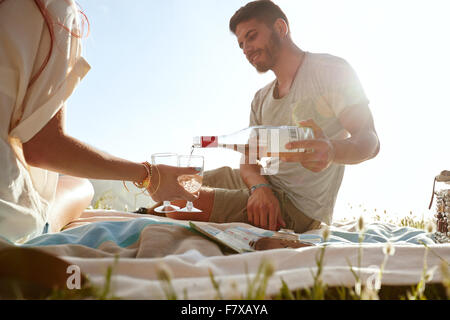 Aufnahme eines jungen Paares, Wein trinken und genießen ein Picknick im Grünen.  Junger Mann mit ihrer Freundin im Urlaub auf dem Rasen sitzen Stockfoto