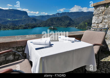 Tabelle mit Emty Platte im Freien serviert. Blick über den See Bled, Insel mit Kirche und Alpen im Hintergrund. Slowenien. Stockfoto