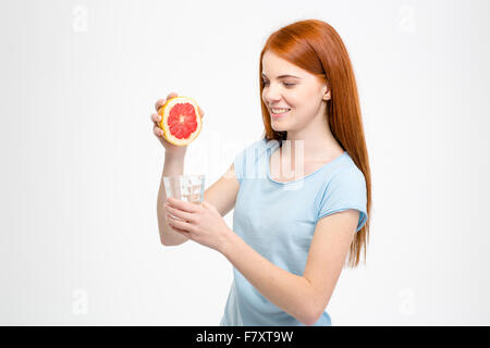 Glücklich lächelnd, schöne junge Frau mit langen roten Haaren drücken Grapefruit-Saft im Glas auf weißem Hintergrund Stockfoto