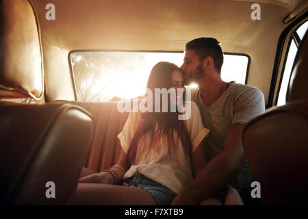 Porträt des entspannten junges Paar sitzt auf der Rückseite Sitz des Autos unterwegs. Mann küssen Stirn seiner Freundin, mit hellen Stockfoto