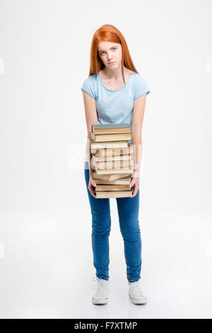 Müde, erschöpft, junge rothaarige Frau stehen und halten Stapel Bücher auf weißem Hintergrund Stockfoto