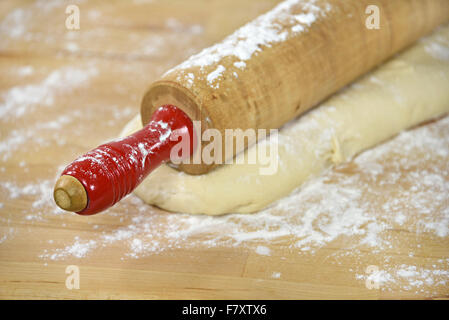 Nahaufnahme von Retro-hölzernen Nudelholz mit rotem Griff auf Brotteig und Mehl. Stockfoto