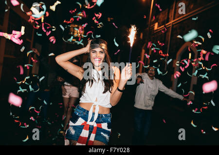 Glückliche junge Frau feiern mit ihren Freunden im Freien in der Nacht. Freunde, Partys im Freien mit Konfetti und Wunderkerzen. Stockfoto