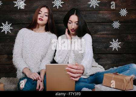 Zwei schöne Mädchen mit einem Tablet, zwischen Geschenke Stockfoto