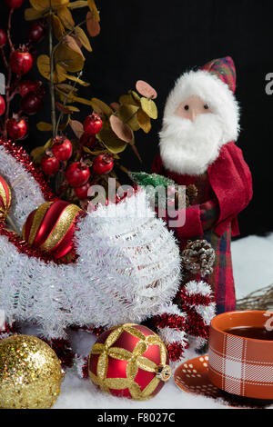 Wohnkultur Santa und seinem Schlitten auf Schnee Baum Dekorationen Tisch setzen und begleitet von einer warmen Tasse Kaffee Stockfoto