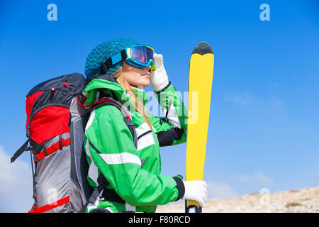 Schöne Skilehrer, Frau tragen Masken und sportliches Outfit hält in der hand ski über blauen Himmelshintergrund Stockfoto