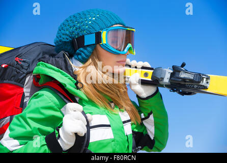 Porträt von niedlichen Skifahrer Mädchen mit sportlichen Maske gelb Ski über blauem Grund halten glücklich Winter aktiv Urlaub zu verbringen Stockfoto