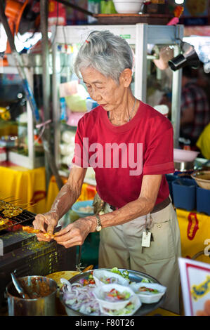 Alte Dame Vorbereitung fleischige Snacks an Chatuchak Weekend Market, Bangkok Stockfoto