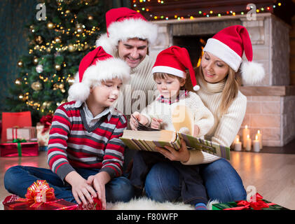 Familie Überprüfung ihrer Fotos im Album Weihnachtsbaum vor Kamin Stockfoto