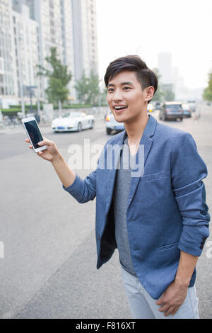 Junger Mann warten auf Taxi mit Smartphone Stockfoto