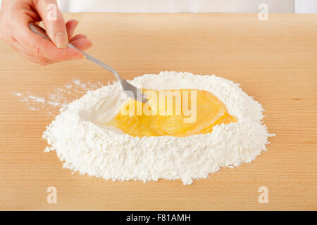 Koch, schlagen von Eiern in Mehl auf Arbeitsplatte für die Herstellung von Teigwaren Stockfoto