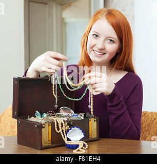 rothaarige Mädchen sieht Schmuck in Schatztruhe zu Hause Stockfoto