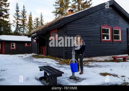 Hübsches Mädchen füllen einen Eimer mit einer Handpumpe aus einem Brunnen außerhalb einer Hütte im Wald nördlich von Oslo - Landschaft Stockfoto