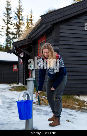 Ziemlich lächelnde Frau eine Handpumpe Pumpen füllen Sie einen Eimer aus einem Brunnen außerhalb einer Hütte im Wald nördlich von Oslo Stockfoto