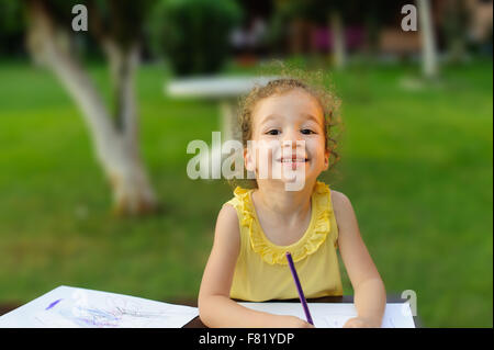 glückliches kleines Mädchen zeichnen etwas in ihrem Notizbuch im Garten Stockfoto
