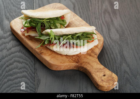 rustikale Sandwiches mit Schinken, Rucola und Tomaten im Fladenbrot auf Holztisch Stockfoto