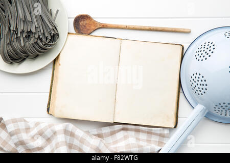 Kochbuch und schwarzen Nudeln mit Sepia-Tintenfischtinte auf weißem Tisch Stockfoto