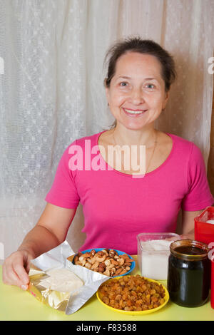 Reife Frau mit Nahrungsmitteln für den Honigkuchen am Küchentisch. Eines der Stadien des Kochens des Honigkuchen.  Serien ansehen Stockfoto