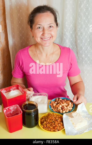 Reife Frau mit Nahrungsmitteln für den Honigkuchen am Küchentisch. Eines der Stadien des Kochens des Honigkuchen.  Serien ansehen Stockfoto