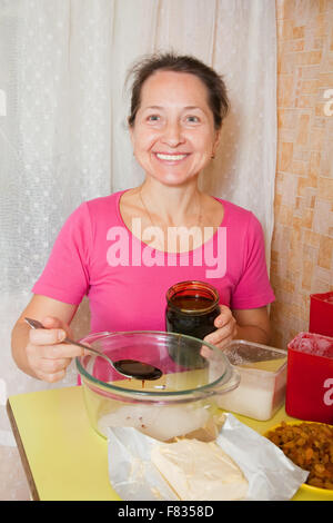 Reife Frau fügt Honig in Schüssel mit Zucker. Eines der Stadien des Kochens des Honigkuchen.  Serien ansehen Stockfoto