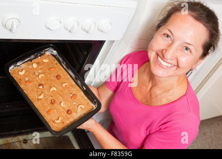 Reife Frau Bräter in Ofen Teig aufsetzen. Eines der Stadien des Kochens des Honigkuchen.  Serien ansehen Stockfoto